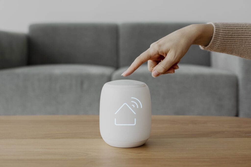 Main interagissant avec un objet connecté IoT à icône domotique lumineuse, symbole de la répartition hardware et software